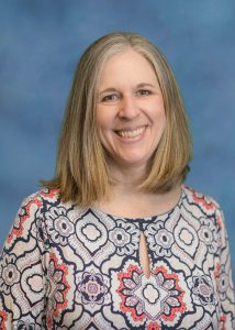 female, blonde hair, blue background, white blue and orange pattered shirt