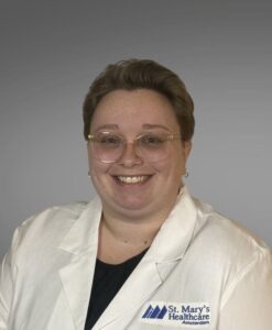 medical provider, female, short blonde hair, glasses, white jacket, black shirt.