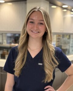 nurse in front of nursing station, blonde hair, blue scrubs